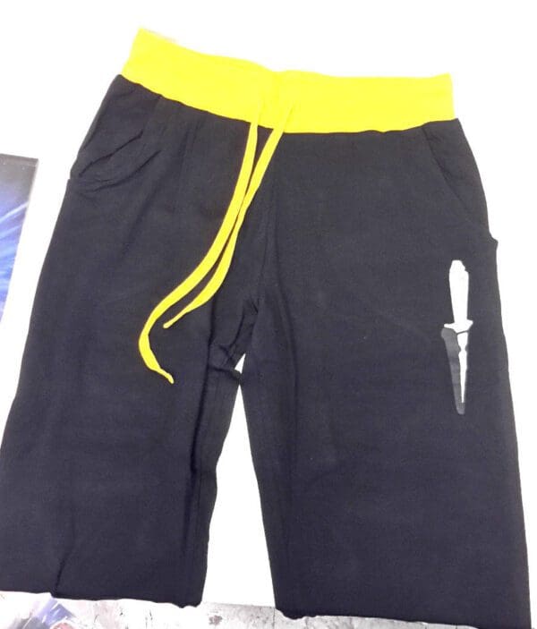 Black sweatpants with yellow waistband and knife design.