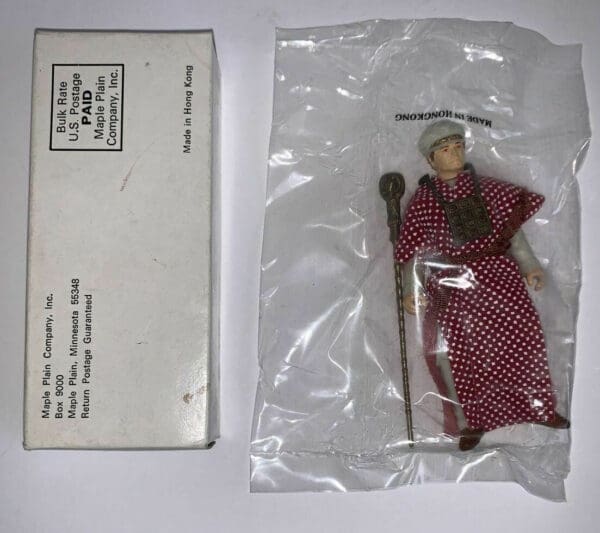 Red-robed figure with a staff in a plastic bag.