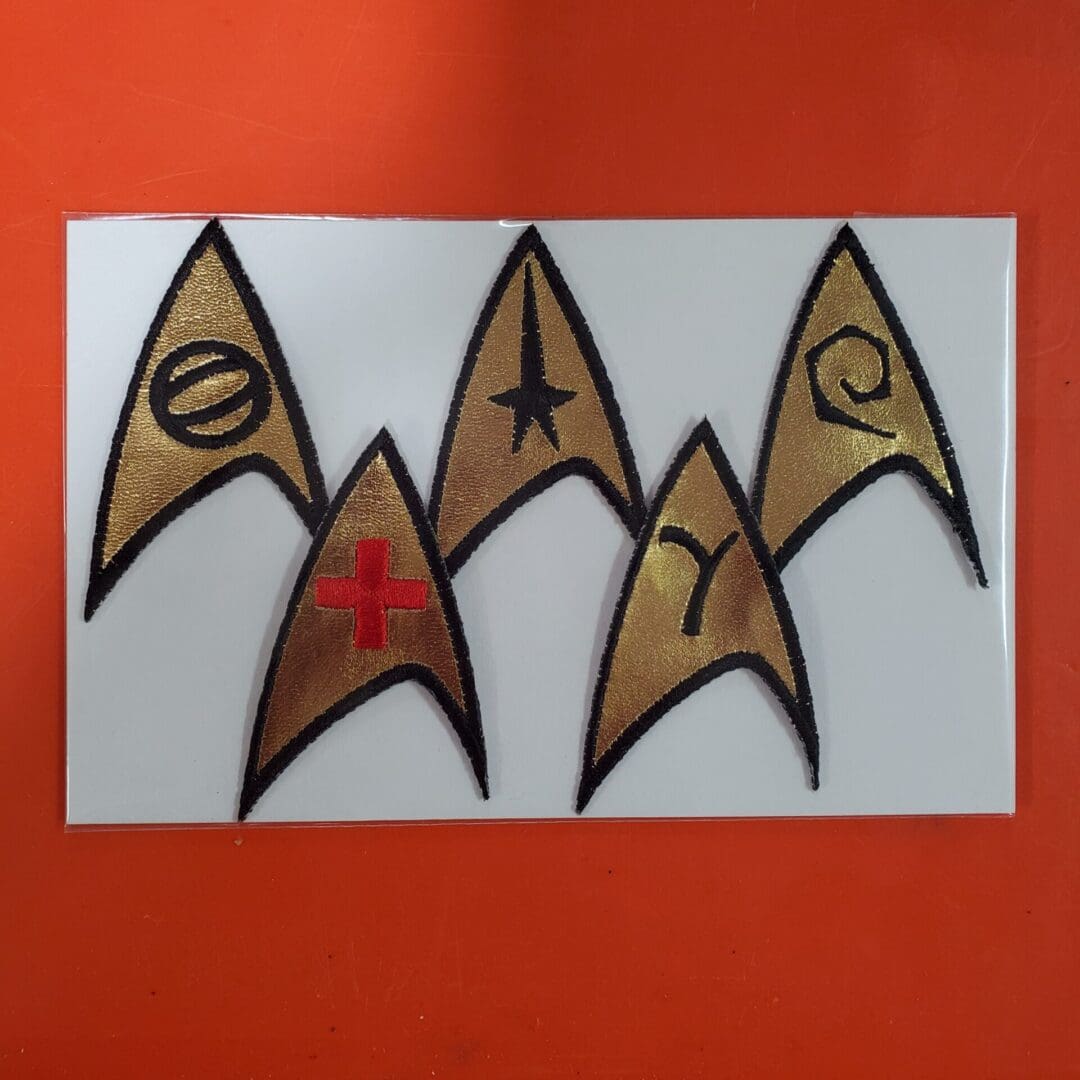 Gold Star Trek insignia patches on white card.