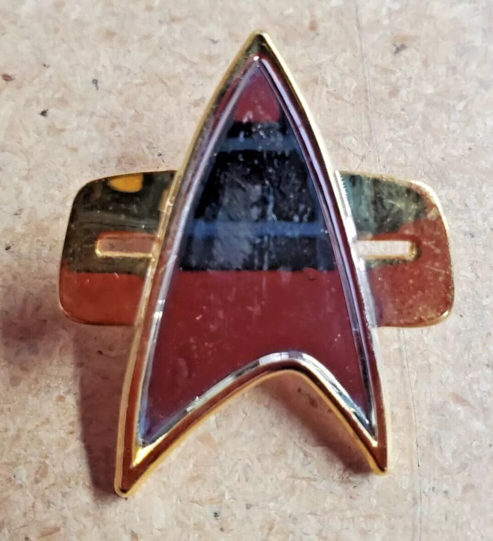 Here's an alt tag for the image: Gold Starfleet insignia pin.